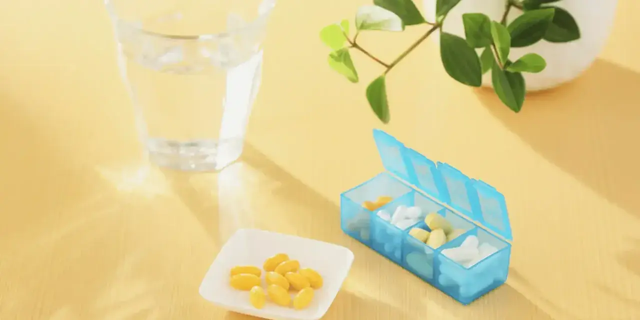 Un bicchiere d'acqua, una ciotolina con capsule gialle e un portapillole blu. Forse integratori per capire cosa sono gli elettroliti.