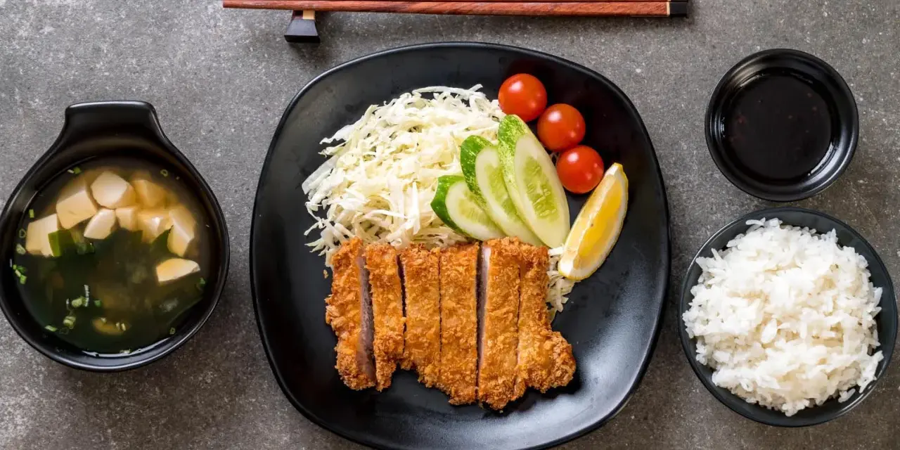 Chrupiące katsu na talerzu z ryżem, zupą miso, warzywami i cytryną. Idealny zestaw do jedzenia pałeczkami.