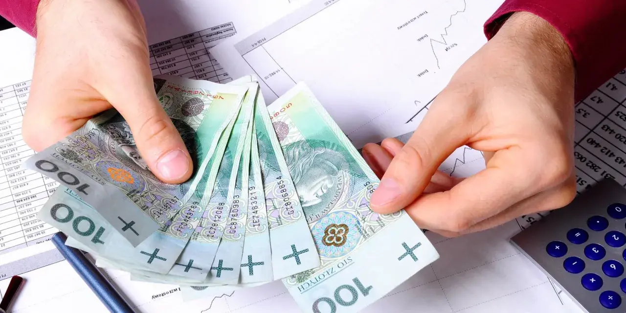 Ręce trzymające polskie stuzłotówki, obok kalkulator i wykresy. Jak wypłacić pieniądze z PPK?