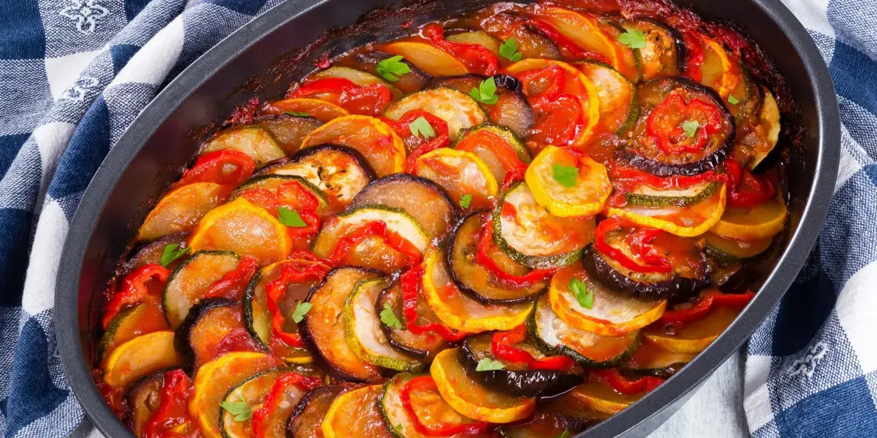 Gotowy ratatouille przepis w naczyniu żaroodpornym, z plasterkami cukinii, bakłażana i pomidorów, polany sosem.