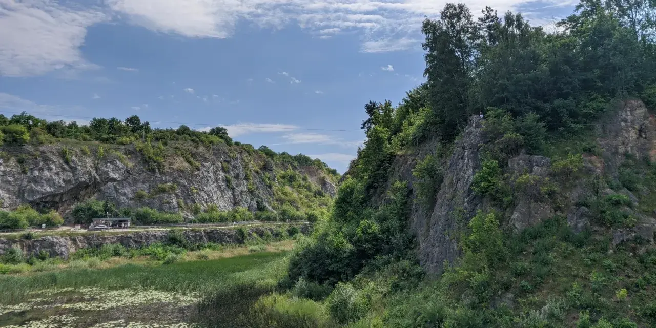 Kamieniołom z wodą i zielenią, skalne zbocza, niebo z chmurami.