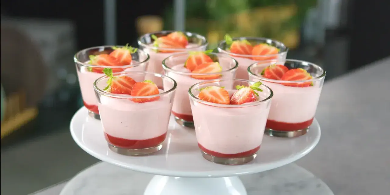 Deliziosi dolci al cucchiaio alla fragola, serviti in bicchierini trasparenti e guarniti con fragole fresche.
