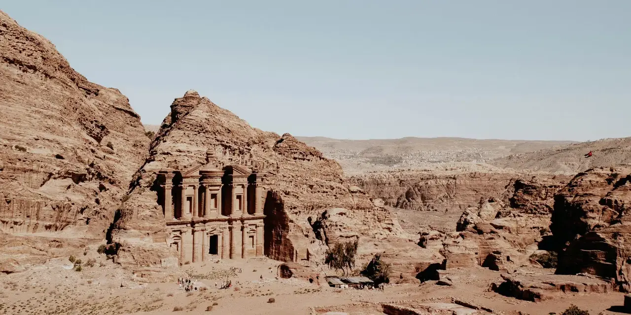 The ancient jordan ruins of Petra, carved into sandstone cliffs, stand majestically under a clear blue sky.