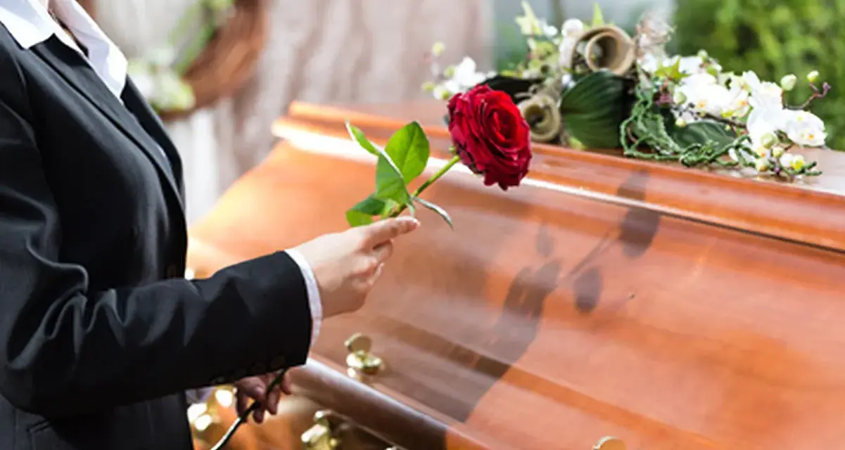 Eine Frau in Trauer legt eine rote Rose auf den Sarg. Sie muss die Beerdigung ihres getrennt lebenden Ehemanns bezahlen.