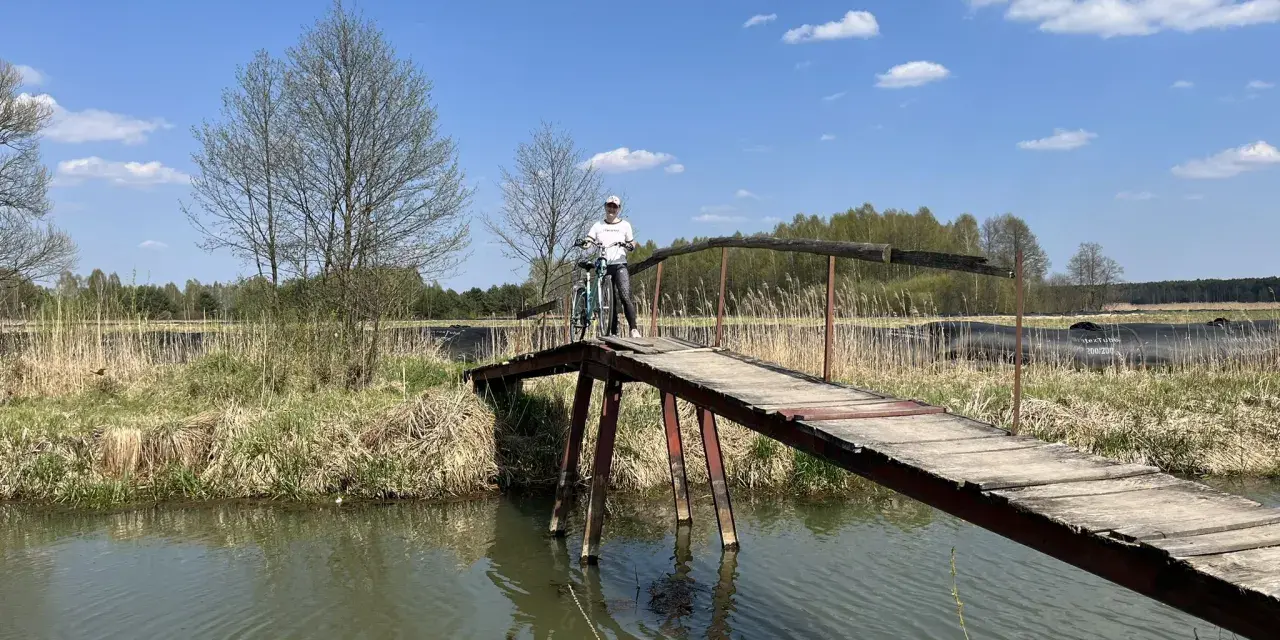 Osoba z rowerem na drewnianym mostku nad rzeką. Piękny dzień na odkrywanie tras rowerowych łódzkiego.