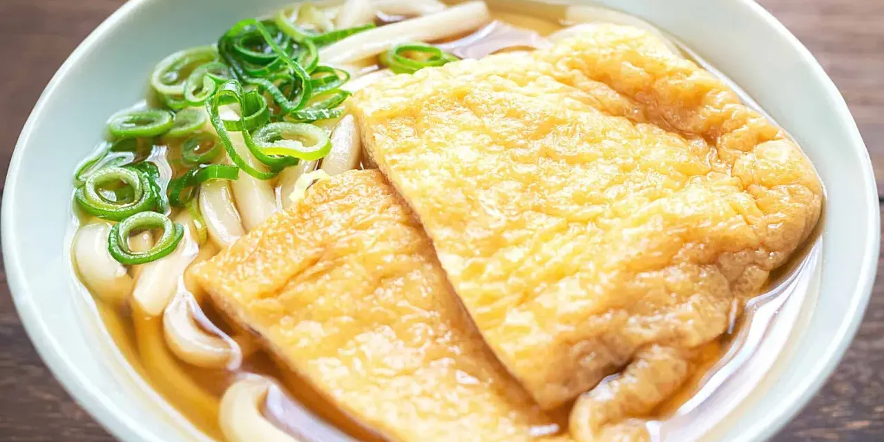 Pyszna zupa z makaronem udon z dwoma kawałkami smażonego tofu i zieloną cebulką.