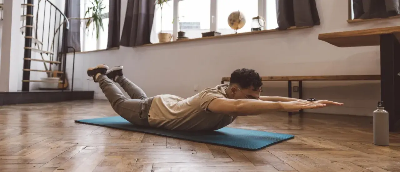 Homme faisant un exercice dos sur un tapis, bras tendus, jambes levées.