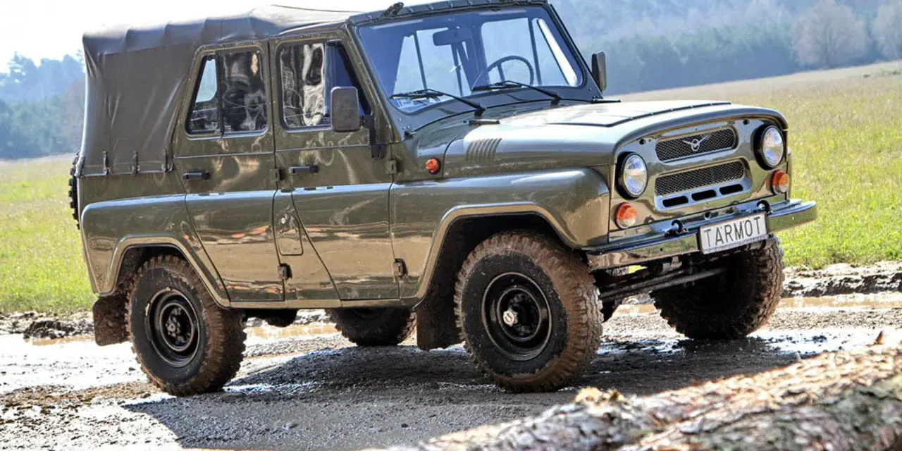 Zielony UAZ z plandeką, marka samochodu na u, pokonuje błotnisty teren.