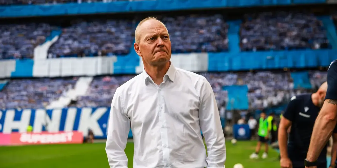 Trener w białej koszuli na tle trybun pełnych kibiców podczas meczu Widzew Łódź – Lech Poznań.