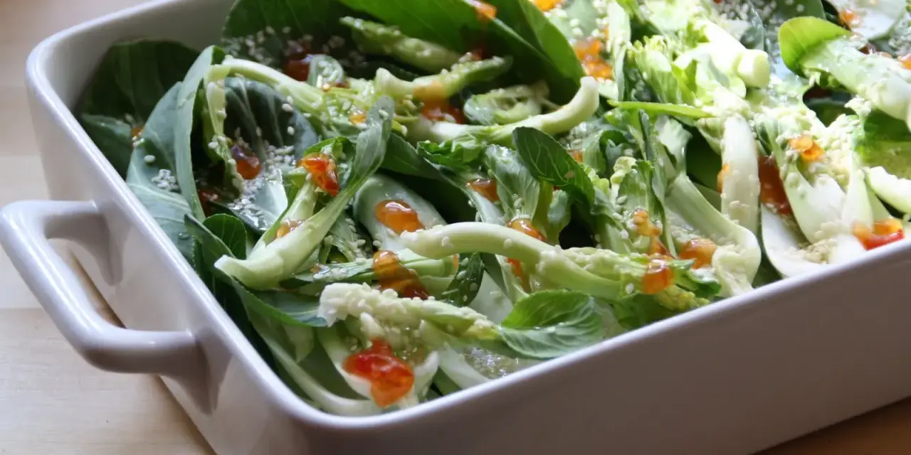 Pyszna kapusta pak choi po tajsku, polana sosem i posypana sezamem, w białej ceramicznej misie.