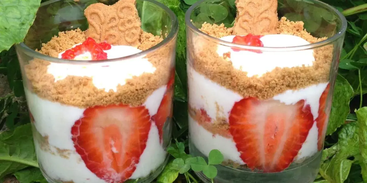 Deux verrines de tiramisu fraises spéculoos, garnies de crème, fraises fraîches et biscuits spéculoos, posées sur un lit de verdure.