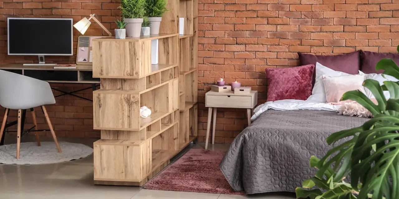 Soluzione d'arredo per un monolocale di 40 mq: libreria divisoria, scrivania, letto accogliente e piante verdi creano uno spazio funzionale e di stile.