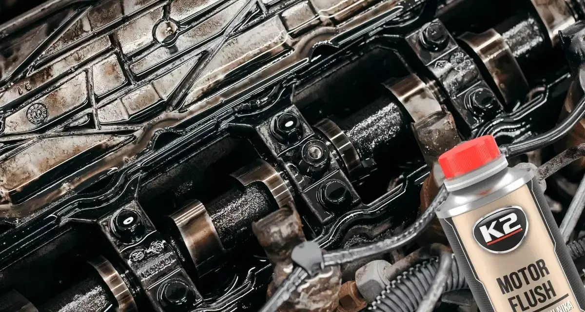 Silnik z widocznymi elementami rozrządu, pokryty czarnym osadem. Obok butelka płukanki K2 Motor Flush, która pomoże rozwiązać problem niskie ciśnienie oleju na rozgrzanym silniku.