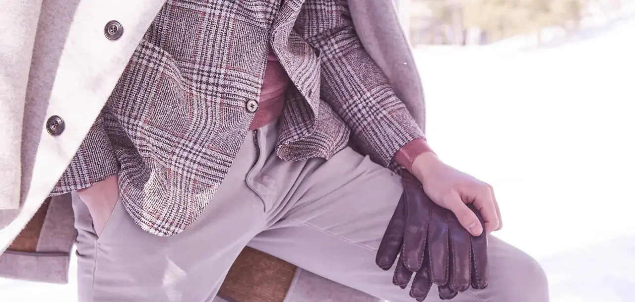 Un uomo indossa un elegante spezzato con giacca a quadri, maglione rosa e guanti in pelle marrone, pronto per l'inverno.