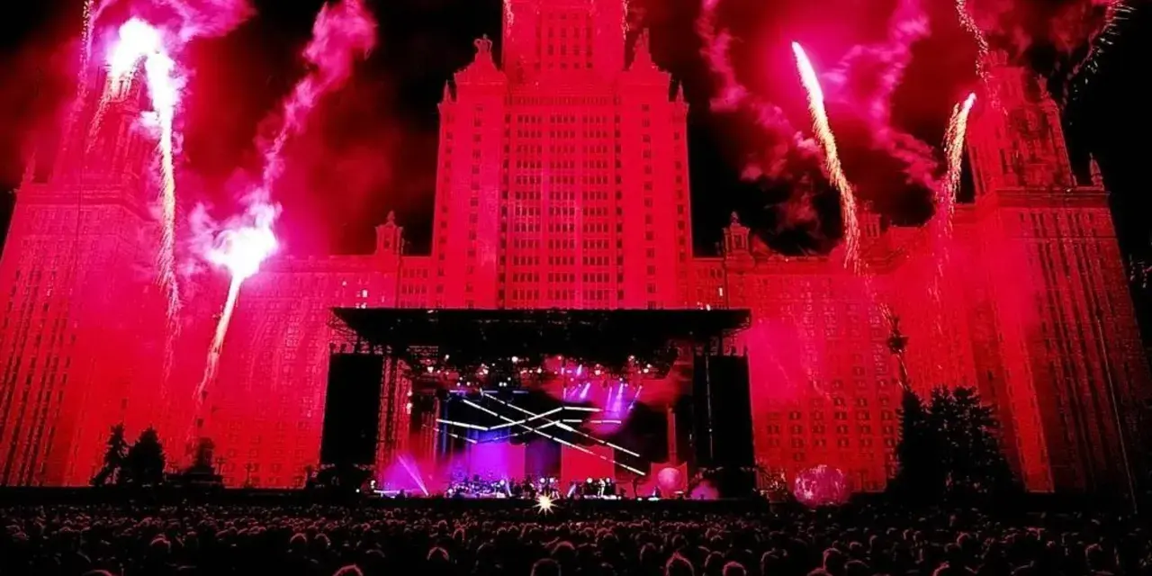Ogromny budynek oświetlony na czerwono, fajerwerki i scena koncertowa. Tłum ludzi czeka na największy koncert na świecie.