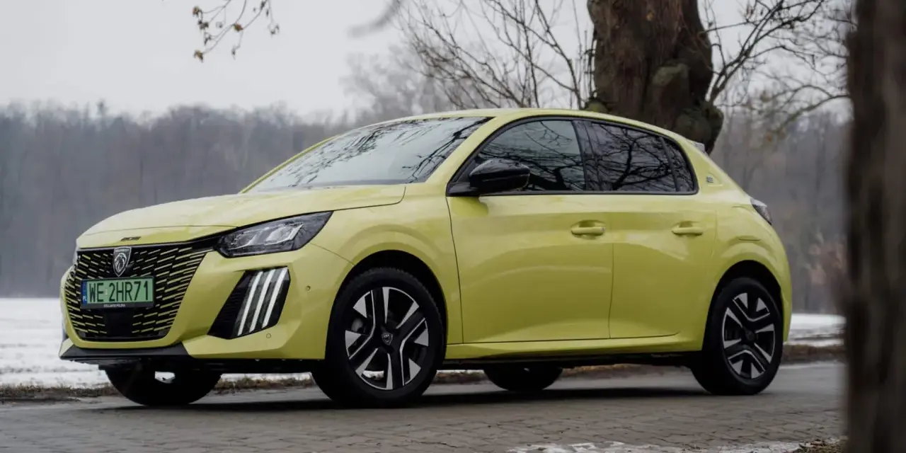 Żółty Peugeot e-208 stoi na tle drzew i zimowego krajobrazu.
