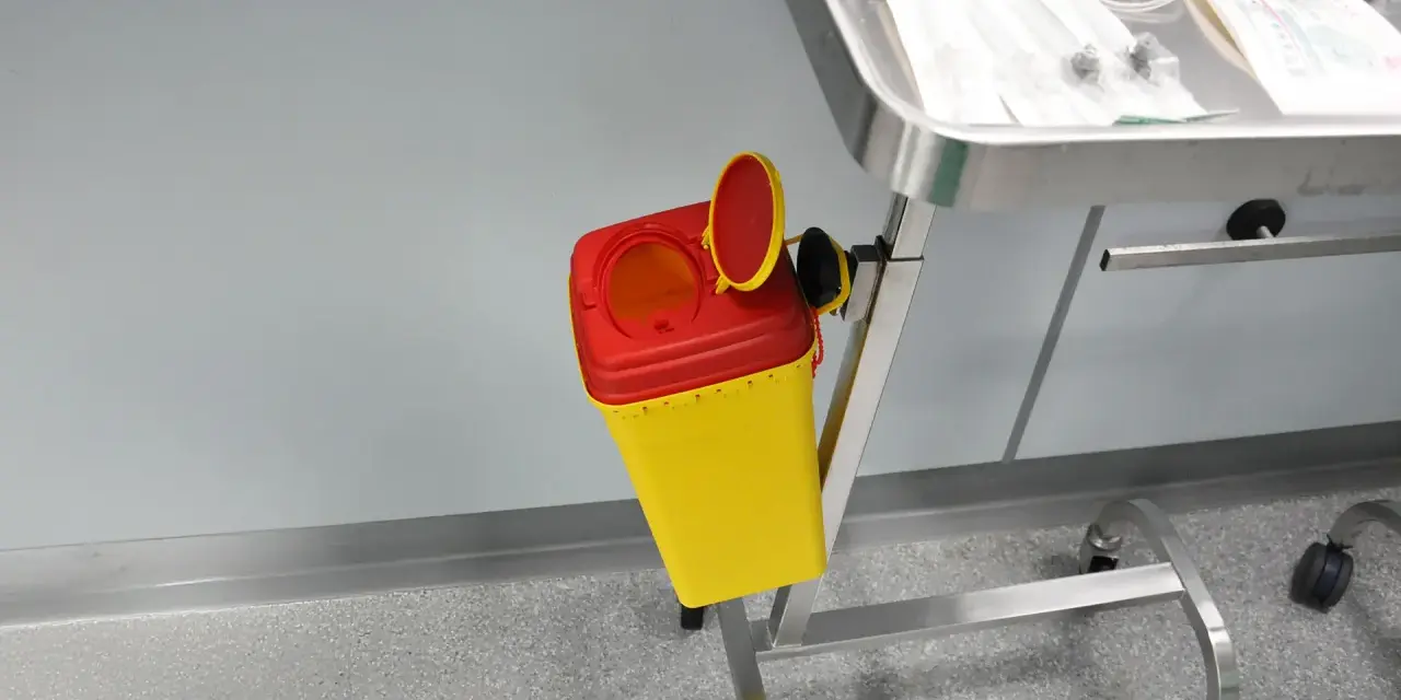 Gelber Behälter mit rotem Deckel für medizinische Abfälle, bereit zur sicheren Entsorgung von Spritzen und Nadeln, um eine Nadel desinfizieren zu können.