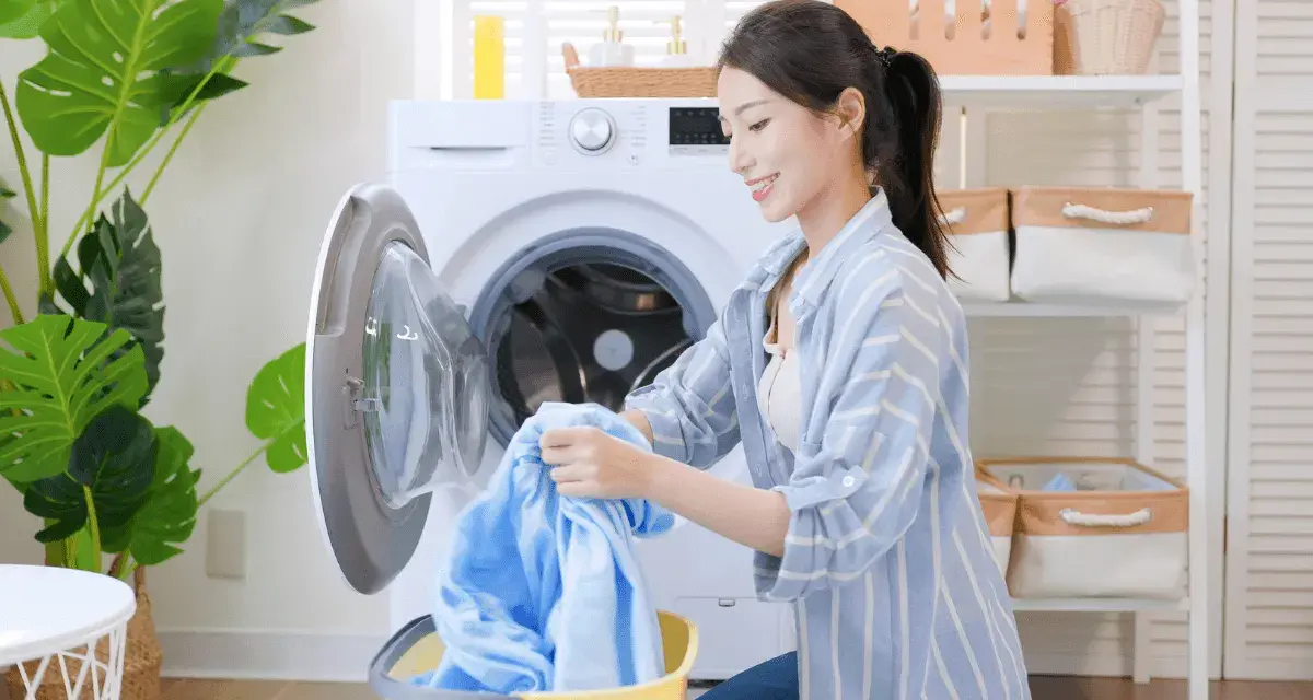 Une femme charge du linge bleu dans une machine à laver. Le cycle de rincage de la machine à laver est terminé.