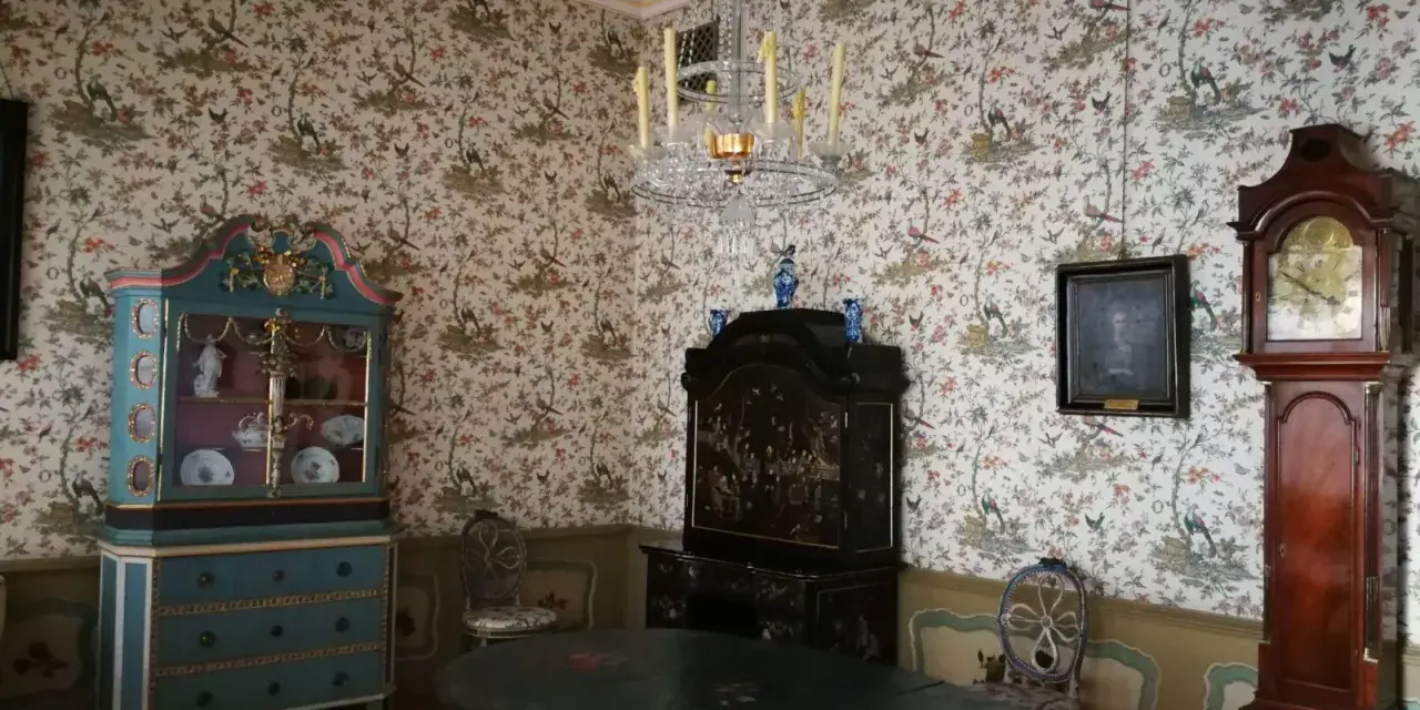 Wnętrze Uphagen House: zabytkowy zegar, szafka, stół i tapeta z ptakami.