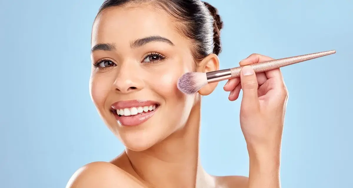 Une femme souriante utilise un pinceau pour appliquer du correcteur maquillage sur sa joue.