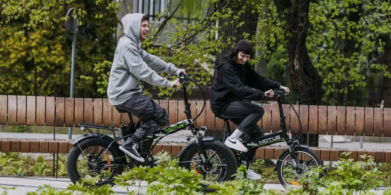 Dwaj młodzi ludzie cieszą się jazdą na rowerach elektrycznych. Dofinansowanie do roweru elektrycznego sprawia, że ekologiczny transport jest dostępny dla każdego.