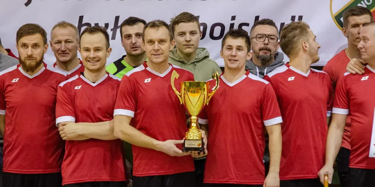 Drużyna w czerwonych koszulkach świętuje zwycięstwo z pucharem. W centrum stoi Andrzej Zaborowski, dumny z sukcesu.