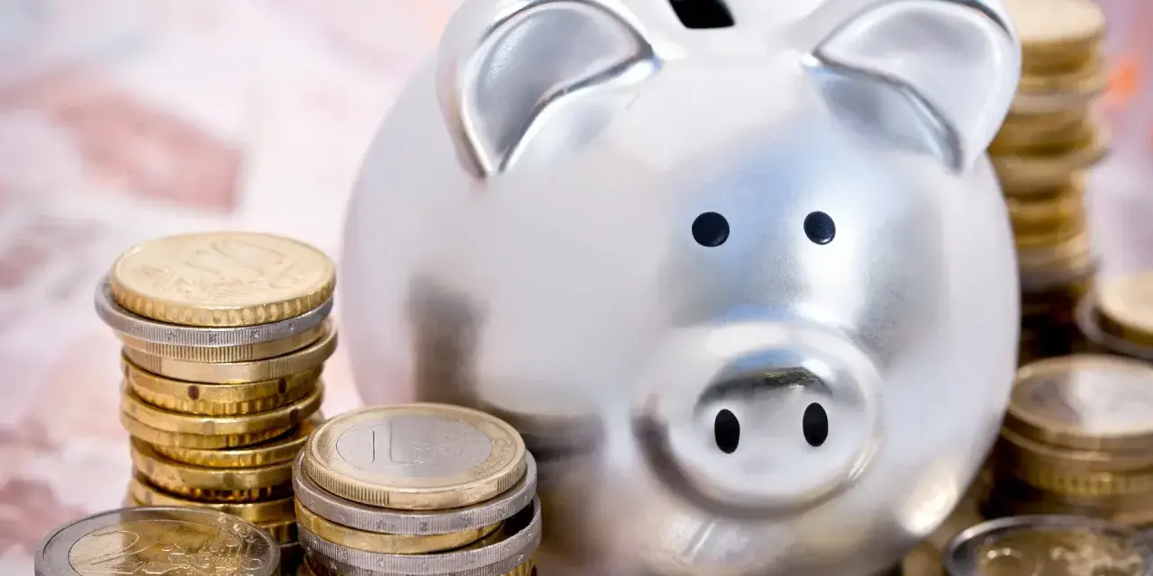Hucha plateada rodeada de pilas de monedas de euro, simbolizando las ventajas del euro para el ahorro.