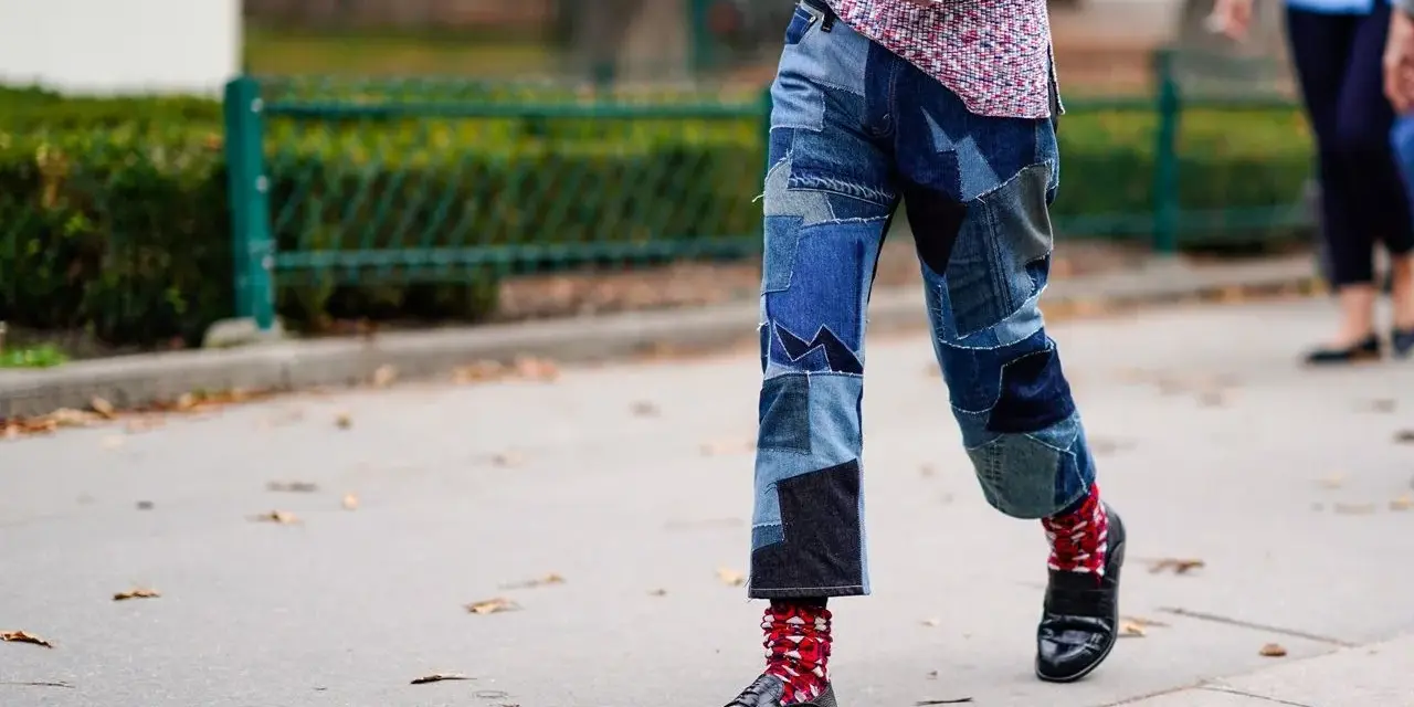 Uomo con jeans patchwork e mocassini neri, calzini rossi a fantasia.
