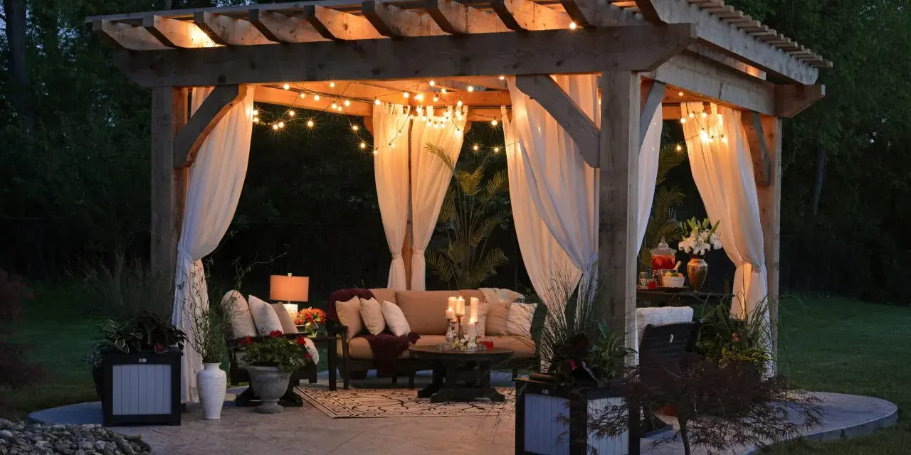 Mysig altan med pergola, draperade gardiner och stämningsfull belysning. Perfekt inspiration för din egen altanbelysning.