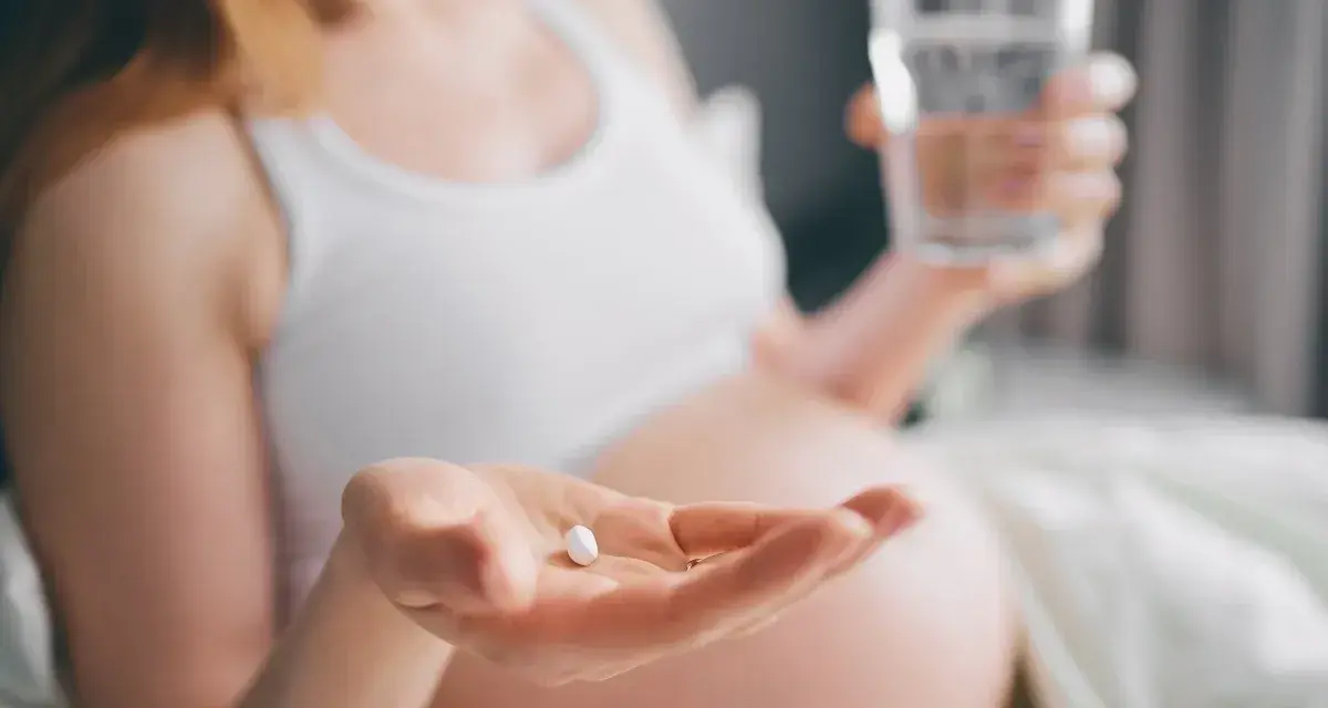 Kobieta w ciąży trzyma tabletkę i szklankę wody. Dba o siebie, przyjmując rutinoscorbin w ciąży.