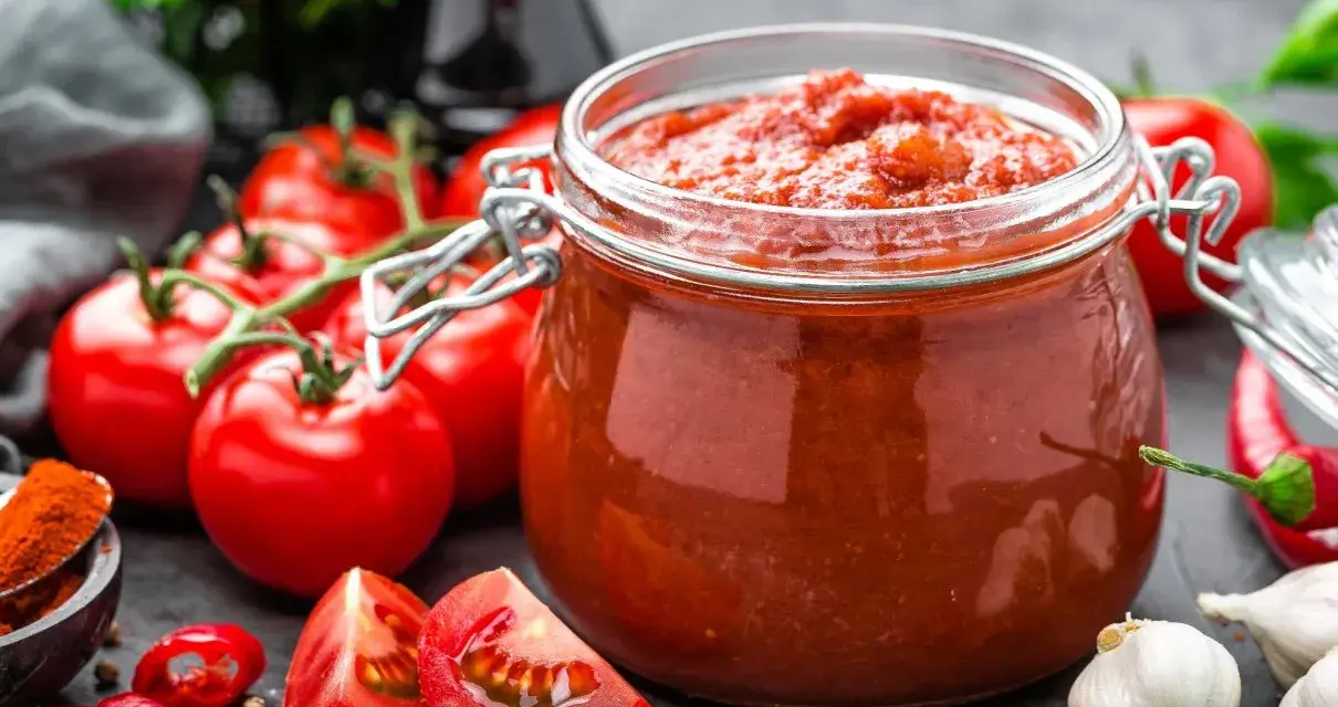 Słoik pełen domowego przecieru pomidorowego, otoczony świeżymi pomidorami, papryczkami chili i czosnkiem. Idealny do sosów i zup.