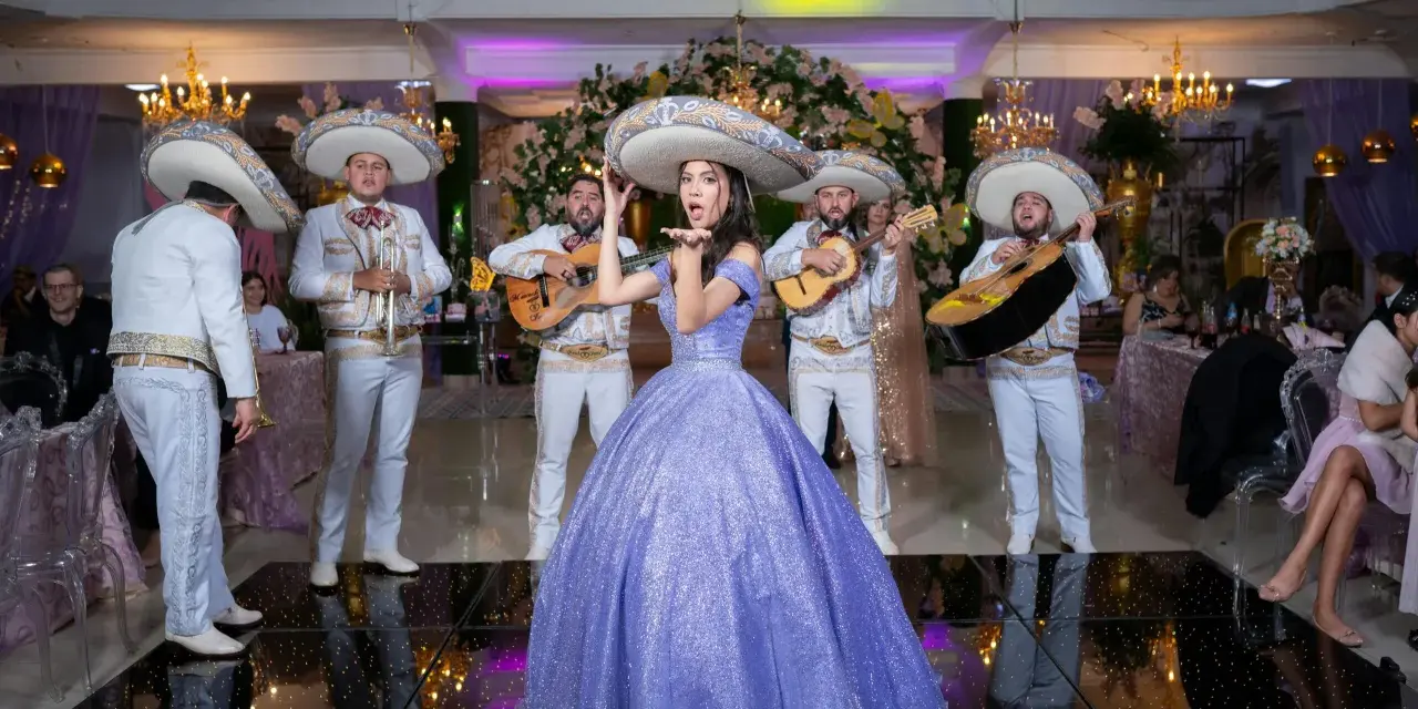 Mariachi grają, a dziewczyna w fioletowej sukni posyła całusy. W tle weselne dekoracje i goście. Idealna sceneria do przyśpiewki weselne tekst.