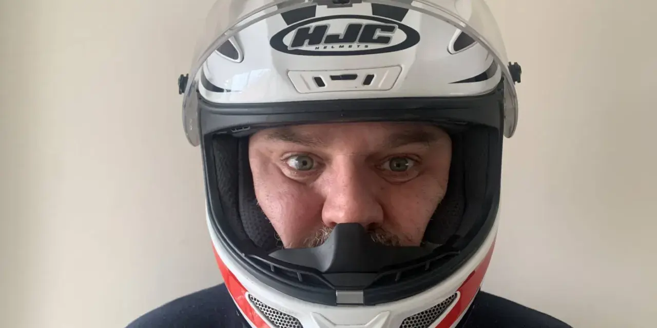 Hombre con casco HJC blanco y rojo, listo para elegir su equipo de moto.
