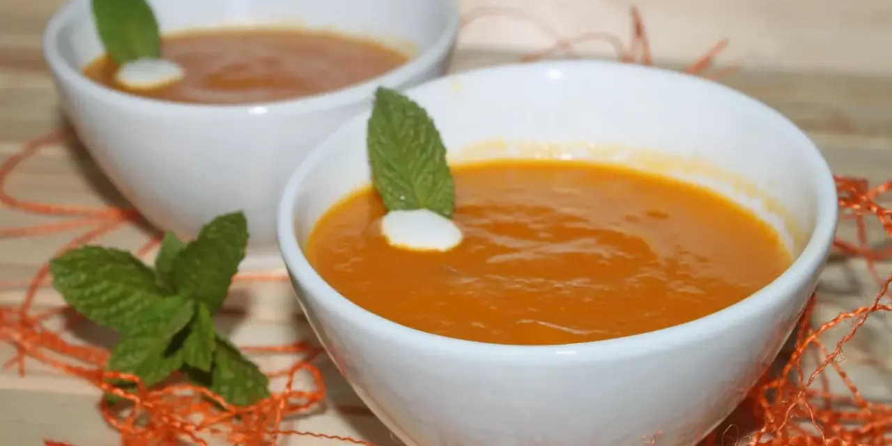 Dos cuencos blancos con crema de calabaza naranja, decorados con menta y un toque de nata.
