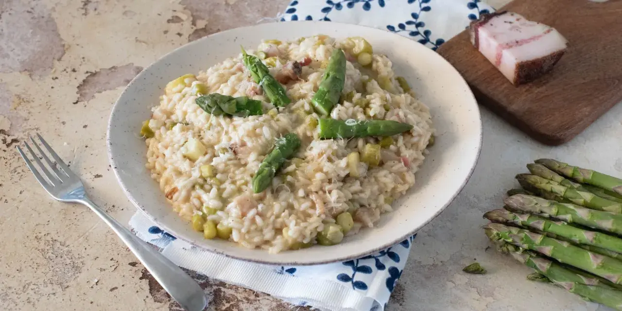 Un cremoso risotto con asparagi e pancetta, guarnito con punte di asparagi freschi e parmigiano.