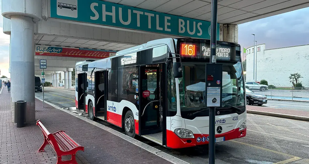 Autobus wahadłowy z otwartymi drzwiami na przystanku lotniskowym, z napisem "SHUTTLE BUS".