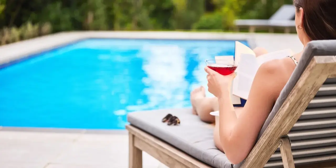 Kobieta z drinkiem i książką relaksuje się przy basenie. Idealne miejsce na wakacje, łatwy kod booking.