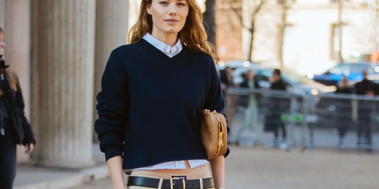 Modello con maglione blu scuro, camicia bianca e pantaloni beige. Un'idea su come vestirsi per uscire con stile.