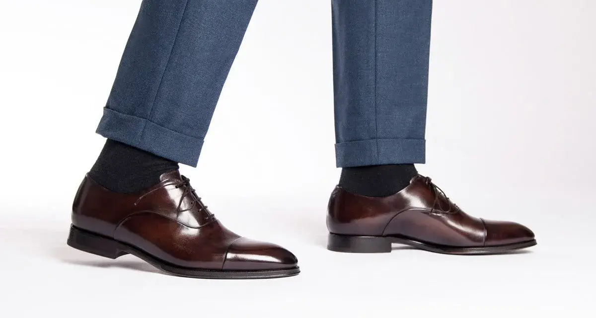 Eleganza senza tempo: un uomo indossa pantaloni blu e scarpe oxford non brogue marroni lucide, perfette per ogni occasione formale.
