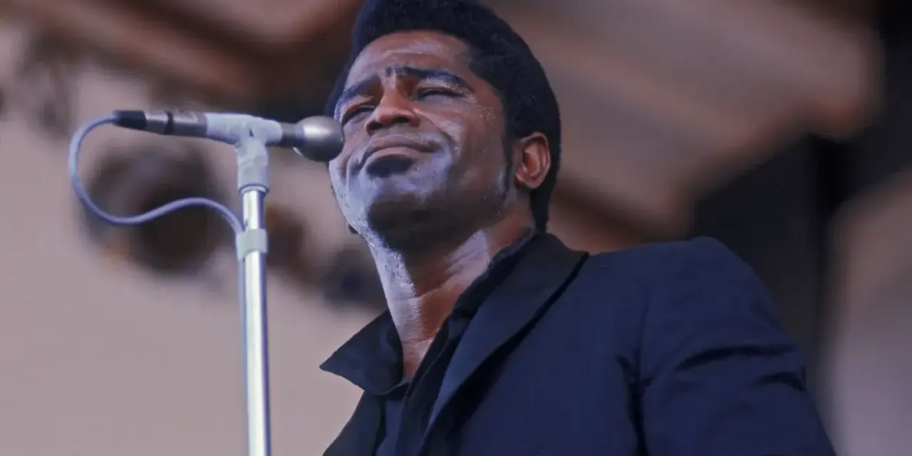 Le chanteur funk français James Brown, en sueur, chante passionnément dans un microphone.