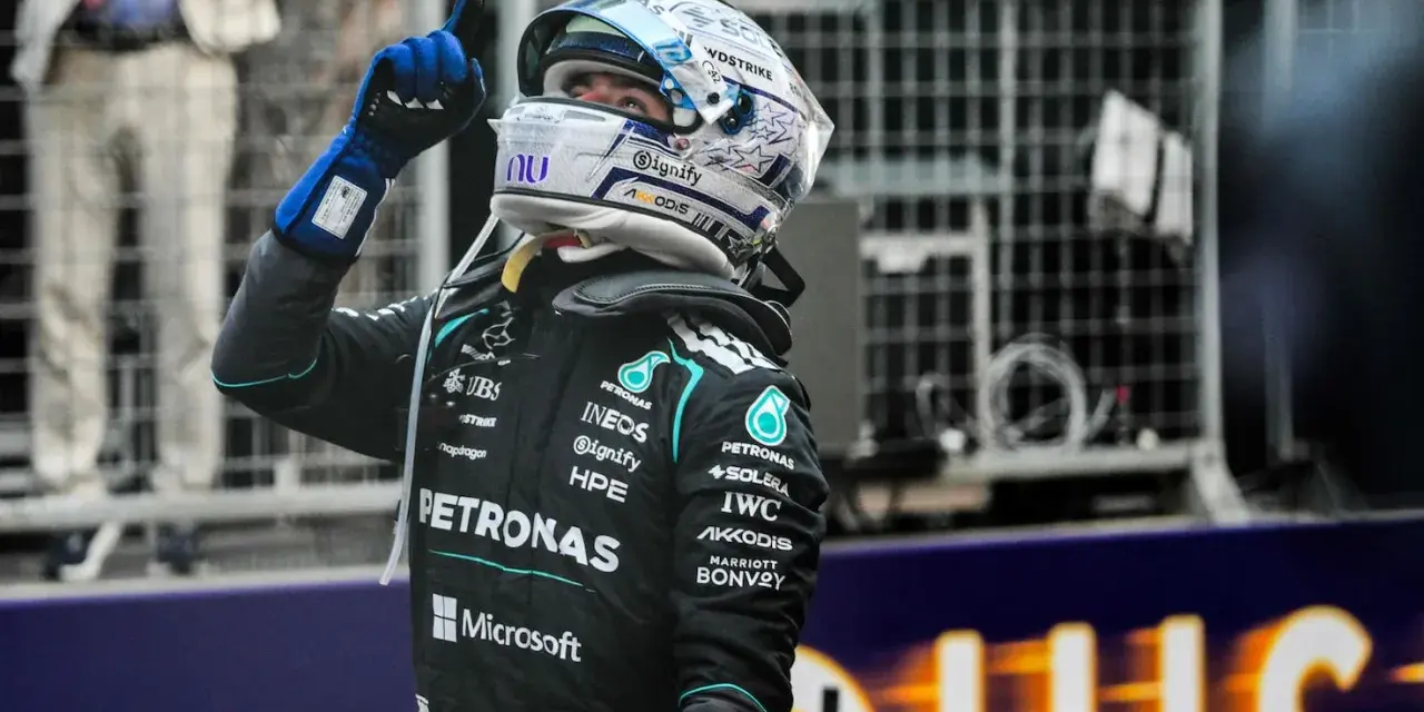 Piloto de F1 con casco y guantes azules levanta el dedo índice, celebrando una victoria en la carrera F1 Mónaco.