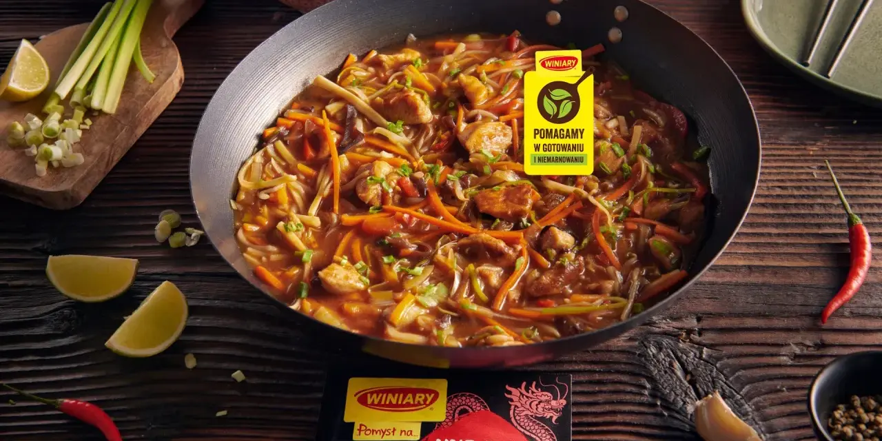 Kurczak w pięciu smakach po chińsku w woku, z warzywami i ryżem w tle. Obok limonki, chili i czosnek.