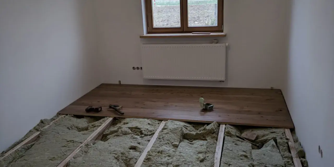 Podłoga na legarach na poddaszu, w trakcie montażu drewnianych desek. Widoczna wełna mineralna izolacyjna.