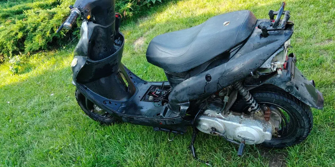 Czarny skuter diesel, nieco zniszczony, stoi na trawie.