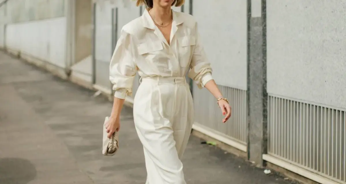 Mujer con un elegante outfit oficina verano: pantalón ancho blanco, camisa holgada y bolso de mano.