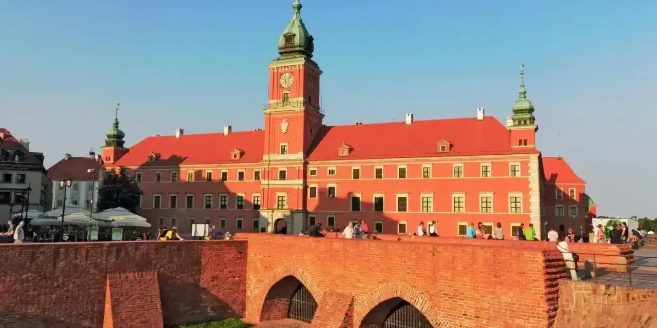 Słoneczny dzień na placu zamkowym w Warszawie. Ludzie odpoczywają na murze przy Zamku Królewskim.