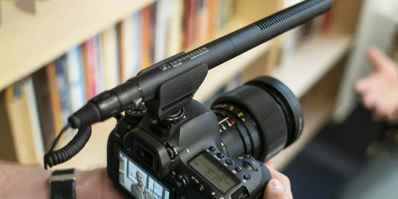 Kamera z mikrofonem kierunkowym Sennheiser MKE 600 na gorącej stopce. Tło to półka z książkami.