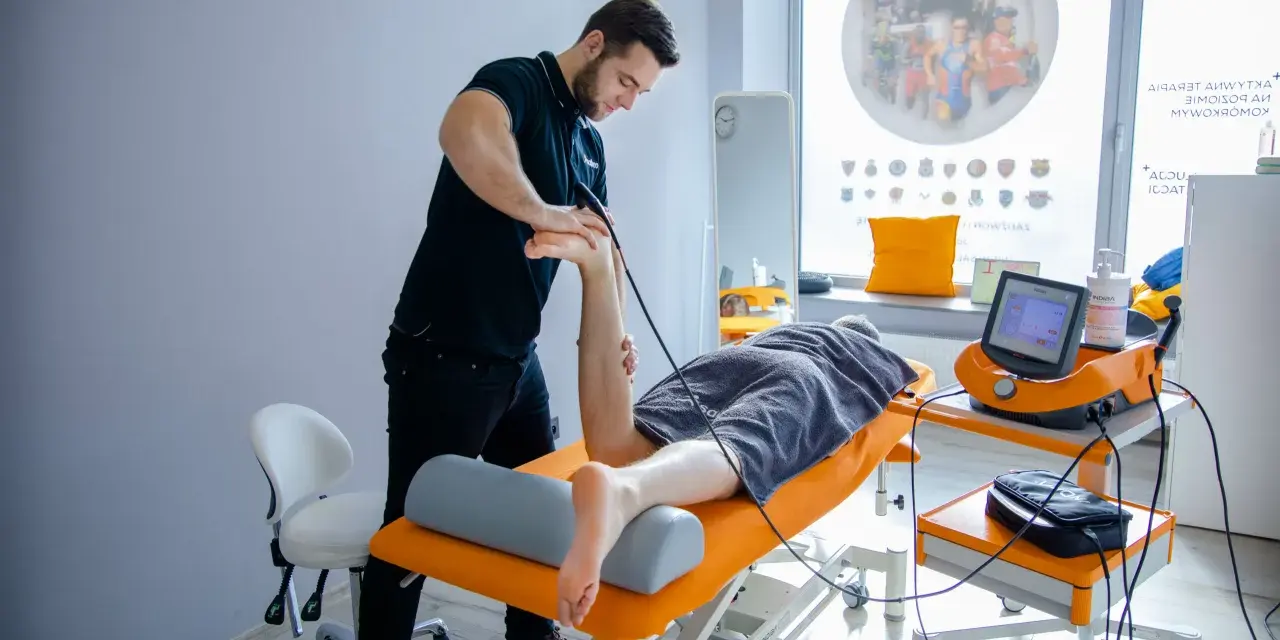 Fizjoterapeuta wykonuje zabieg naświetlania kręgosłupa pacjentowi leżącemu na kozetce.