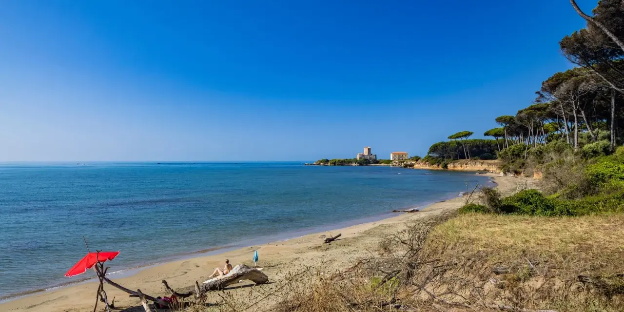 Torre Astura e la sua spiaggia, con un ombrellone rosso e una persona che si rilassa su un tronco.