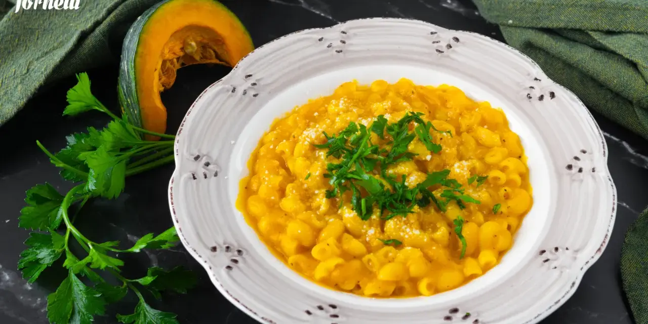 Piatto di pasta e zucca alla napoletana, guarnito con prezzemolo fresco e parmigiano. Accanto, una fetta di zucca e un mazzetto di prezzemolo.